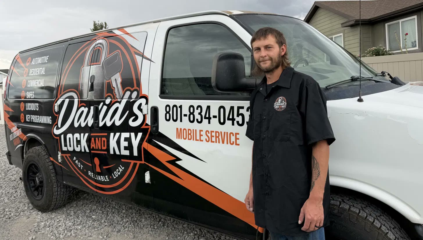 David Smith, owner of David's Lock and Key, standing in a branded work shirt beside his wrapped mobile locksmith van showing the phone number 801-834-0453
